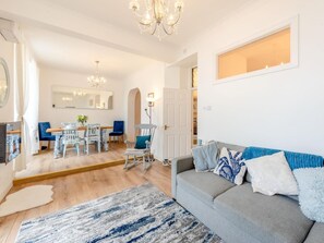 Ein geräumiges Wohnzimmer mit grauem Sofa, einem Essbereich mit Holztisch und Stühlen sowie einem Kronleuchter.