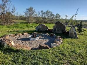 Un foyer circulaire en pierre, avec un récipient métallique au centre, entouré de rochers et d’herbe.