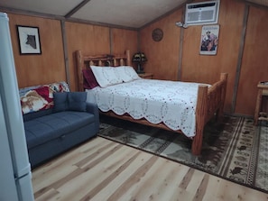 Una habitación con cama, sofá, una mesita y aire acondicionado instalado en la pared.