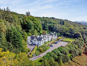 A large, white, multi-story building with a symmetrical facade, surrounded by lush greenery and hills. - 3 Bed in Ambleside (oc-81068) (Claife)