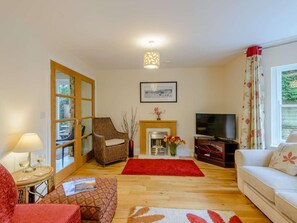 A living room with a fireplace, a television, a sofa, a wicker chair, and a dining table. - 3 Bed in Buxton (oc-81127) (Buxton)