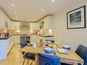 A modern kitchen with white cabinets, a dining table set for breakfast, and a framed picture on the wall. - 3 Bed in Buxton (oc-81127) (Buxton)