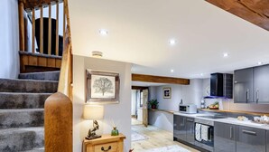 A modern kitchen with a central island, wooden staircase, and a small side table with a lamp and decorative items. - 2 Bed in Crediton (oc-81228) (East Worlington)