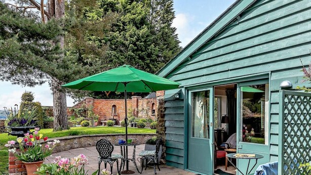 Een terras met buitenmeubels, een groene parasol en een tuin met tulpen.