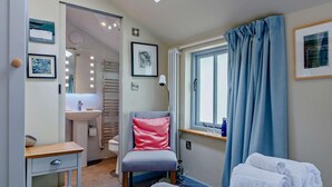 Een slaapkamer met een bed, een stoel, een bureau, een raam met gordijnen, een wastafel en een spiegel.