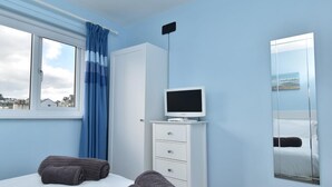 Et hotelværelse med seng, fjernsyn på et stativ, et skab, et vindue med gardiner og et spejl.