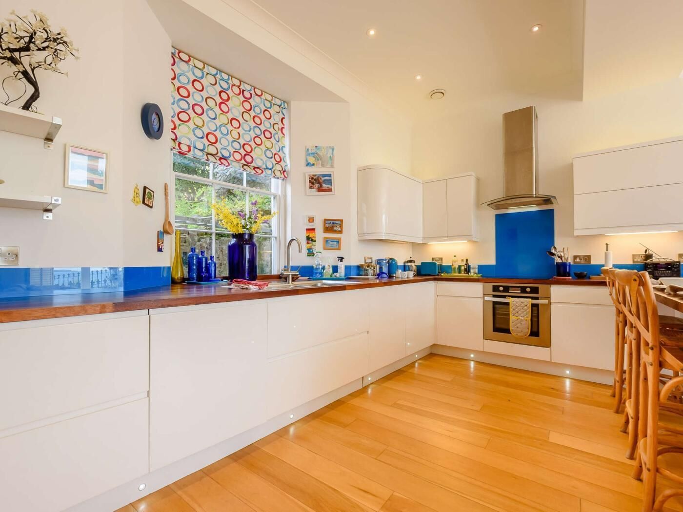 Una cocina moderna con armarios blancos, encimera azul y un ventanal con un diseño circular y colorido.