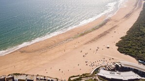 Ein Luftbild einer Strandlandschaft mit einem bogenförmigen Gebäude, vermutlich ein Hotel, das einen uneingeschränkten Blick auf den Ozean und die entfernte Küstenlinie bietet.