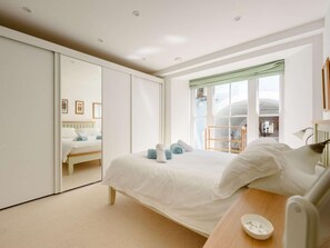 A bedroom with a bed, a bedside table, a mirror, and a window with a view. - 3 Bed in Tenby (oc-fb301) (Tenby)