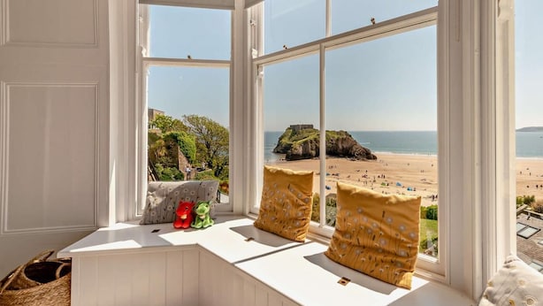 Ein Erker mit Blick auf einen Strand, ein Korbwannenstuhl und zwei Kissen.