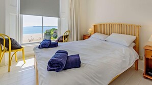 Ein Schlafzimmer mit Bett, Sessel, Nachttisch und Blick auf den Strand.