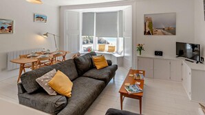 Ein Wohnzimmer mit Sofa, Couchtisch, Esstisch und Fernseher.