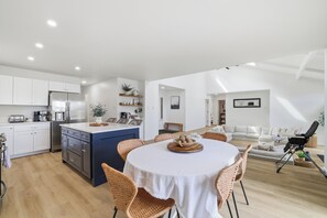 A modern kitchen with white cabinets, a blue island, and a dining area with wicker chairs and a white tablecloth. - Magical Lakefront Memories: Private Dock, Hot tub, and Magnificent Views (Blakeslee)