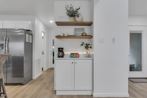 Eine moderne Küche mit einem Edelstahlkühlschrank, weißen Schränken, Holzregalen und einer Kaffeemaschine.