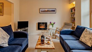 Una sala de estar con dos sofás, una mesa de centro, una chimenea, un televisor y una estantería.
