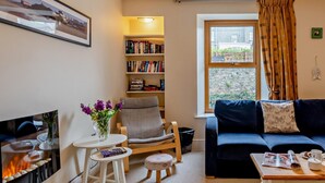 Una sala acogedora con chimenea, una estantería, un sofá y una ventana con cortinas.