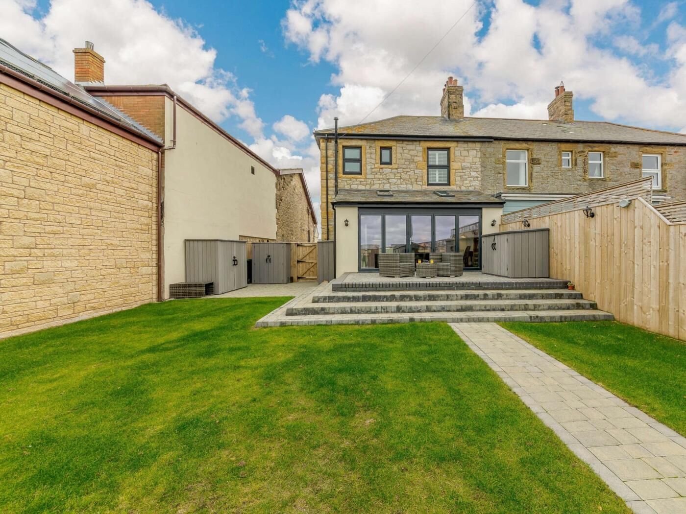 A residential property with a stone facade, a grassy backyard, and a front entrance with steps leading to a covered patio area.
