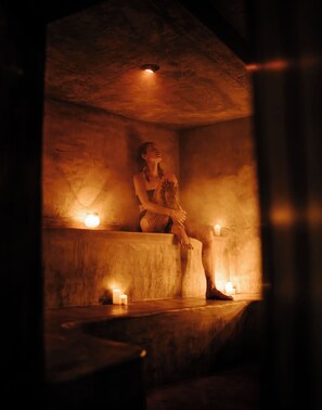 A dimly lit room with a person sitting on a bench, candles, and a stone wall. - Samaya Lush Lakeside Apt - White Lotus (San Miguel)