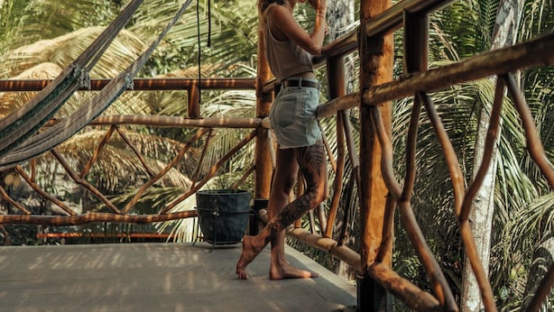A person standing under a bamboo structure with a hammock and palm trees in the background. - Samaya Lush Lakeside Apt - White Lotus (San Miguel)
