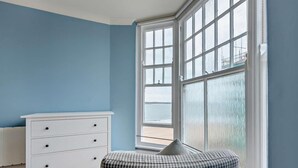 A room with a bay window, a white dresser, and a checkered ottoman. - 1 Bed in Tenby (oc-fb179) (Tenby)