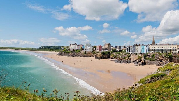 A coastal town with a sandy beach, a clear blue sky, and buildings along the shore. - 1 Bed in Tenby (oc-fb179) (Tenby)