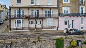 A row of multi-story buildings with balconies, a stone wall, and a paved street. - 1 Bed in Tenby (oc-fb179) (Tenby)