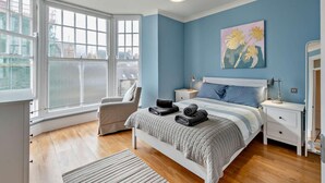 A bedroom with a large window, a bed with a headboard, bedside tables, and a hanging light fixture. - 1 Bed in Tenby (oc-fb179) (Tenby)