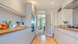 A narrow kitchen with wooden countertops, white cabinetry, and a view into the dining area. - 3 Bed in Tenby (oc-fb174) (Tenby)