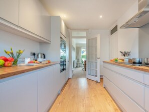 A narrow kitchen with wooden countertops, white cabinetry, and a view into the dining area. - 3 Bed in Tenby (oc-fb174) (Tenby)