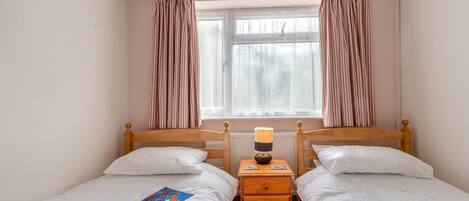 A bedroom with two single beds, a bedside table with a lamp, and a window with curtains.