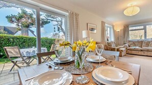 A dining area with a table set for four, a sofa, and a view of the garden. - 3 Bed in Tenby (oc-fb174) (Tenby)