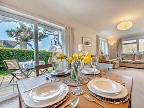 A dining area with a table set for four, a sofa, and a view of the garden. - 3 Bed in Tenby (oc-fb174) (Tenby)