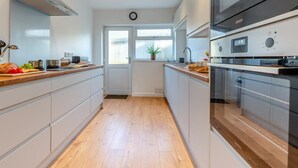 A modern kitchen with a central island, built-in oven, and a window with a view. - 3 Bed in Tenby (oc-fb174) (Tenby)