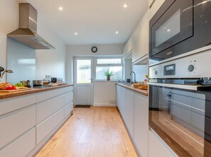 A modern kitchen with a central island, built-in oven, and a window with a view. - 3 Bed in Tenby (oc-fb174) (Tenby)