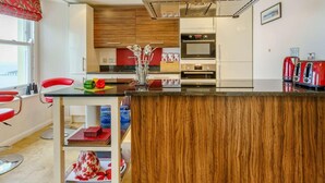 A modern kitchen with a wooden island, stainless steel appliances, and red chairs. - 3 Bed in Tenby (oc-fb273) (Tenby)