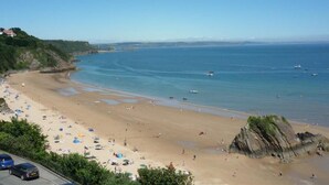 A coastal beach with umbrellas, a rocky outcrop, and boats in the water. - 3 Bed in Tenby (oc-fb273) (Tenby)