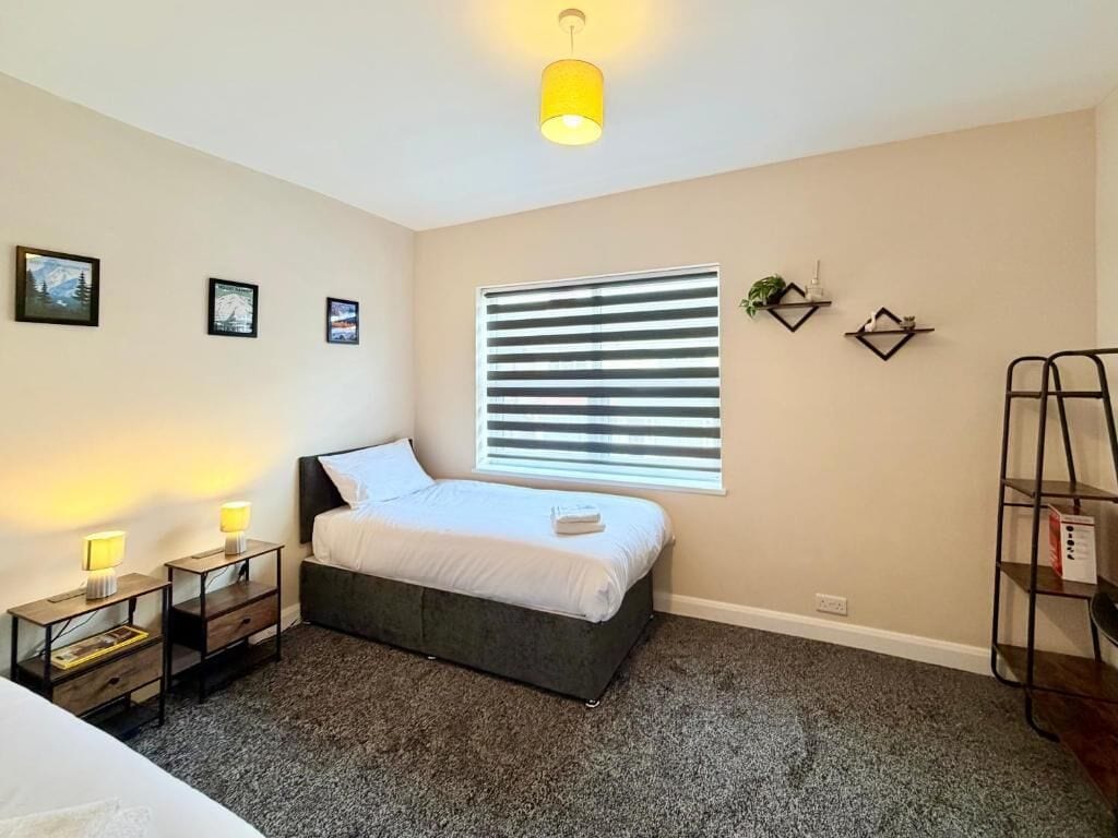 Un dormitorio con cama, lámparas de noche, una ventana con persianas, un estante pequeño y una lámpara colgante.