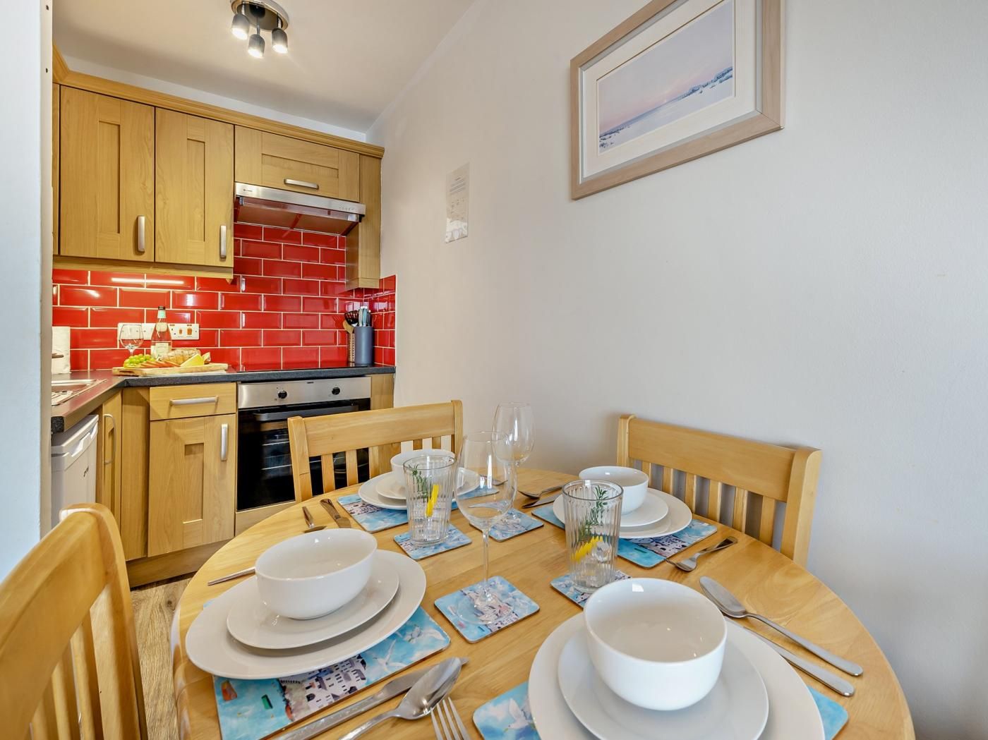 A dining area with a wooden table set for four, surrounded by wooden chairs.