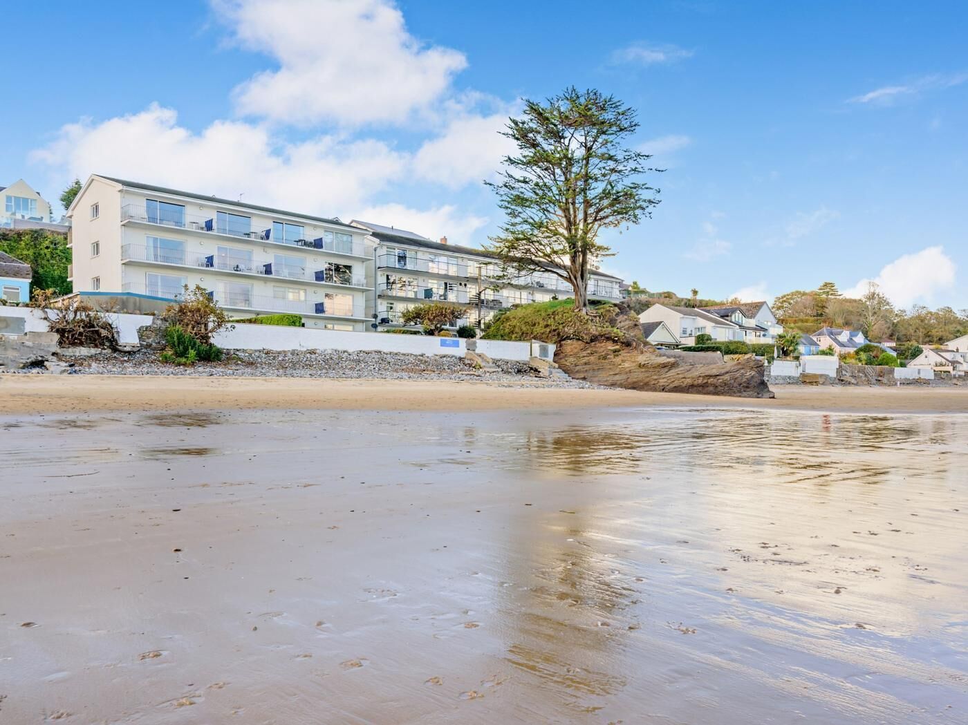 Ein Hotel direkt am Strand mit mehreren Etagen, einem Baum davor und einem Sandstrand.