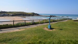 Vista costeira com praia, cerca e área gramada.