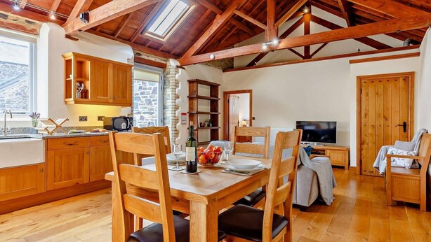 Uma cozinha acolhedora com armários de madeira, uma mesa de jantar com cadeiras, uma televisão e uma parede de pedra.