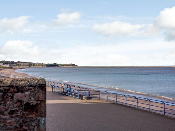 Eine Uferpromenade mit einer Steinmauer, blauen Geländern und Blick auf das Meer.