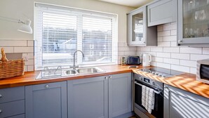 Eine moderne Küche mit grauen Schränken, einer Holz Arbeitsplatte, einem Einbauofen, einer Mikrowelle und einem Fenster mit Jalousien.