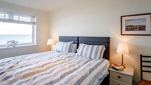Ein Schlafzimmer mit einem Bett, zwei Nachttischlampen, einem Nachttisch, einem Sessel, einem Fenster mit Jalousien und einem gerahmten Bild an der Wand.