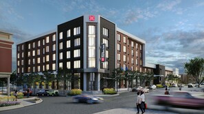 A multi-story hotel with a prominent logo, a large entrance, and a parking area with cars.