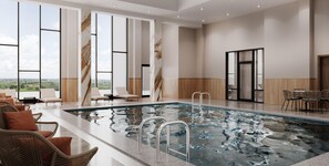 A modern indoor pool area with clear glass walls, lounge chairs, and a view of the landscape.