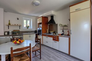 A kitchen with a dining table, chairs, a fruit basket, a stove, a sink, and a refrigerator. - Gite de Pierre, a vacation rental in a restored farmhouse. In the heart of the Périgord Noir (Carsac-Aillac)