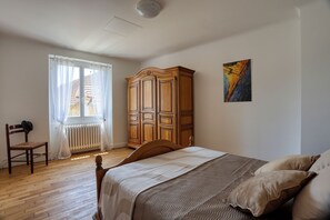 A bedroom with a bed, a wooden wardrobe, a radiator, a window with curtains, and a painting on the wall. - Gite de Pierre, a vacation rental in a restored farmhouse. In the heart of the Périgord Noir (Carsac-Aillac)