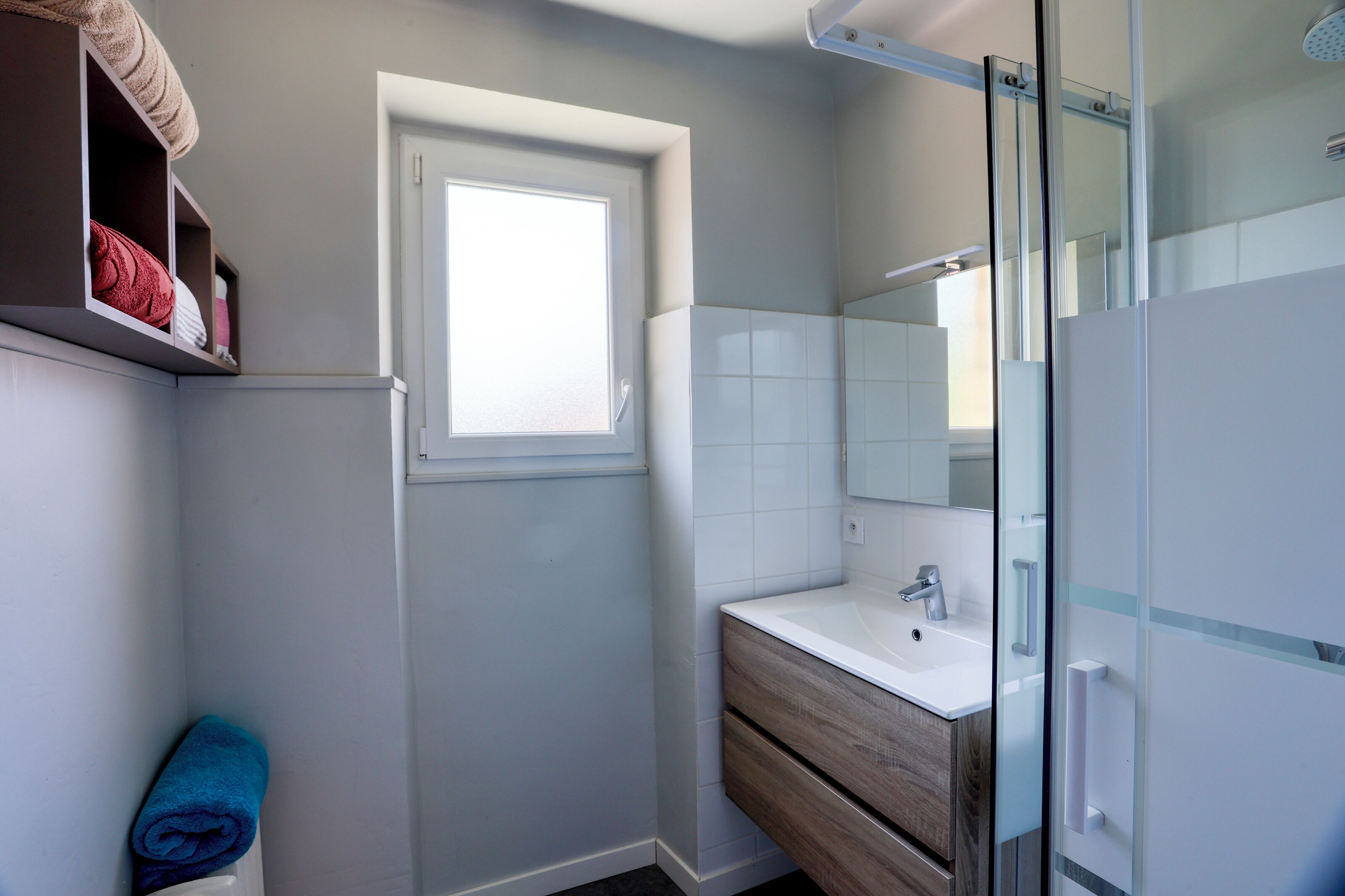 A bathroom with a window, a sink, a mirror, and a towel rack.