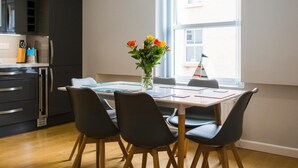 Een moderne keuken met donkere kasten, een eettafel met stoelen en een raam met uitzicht op gebouwen.